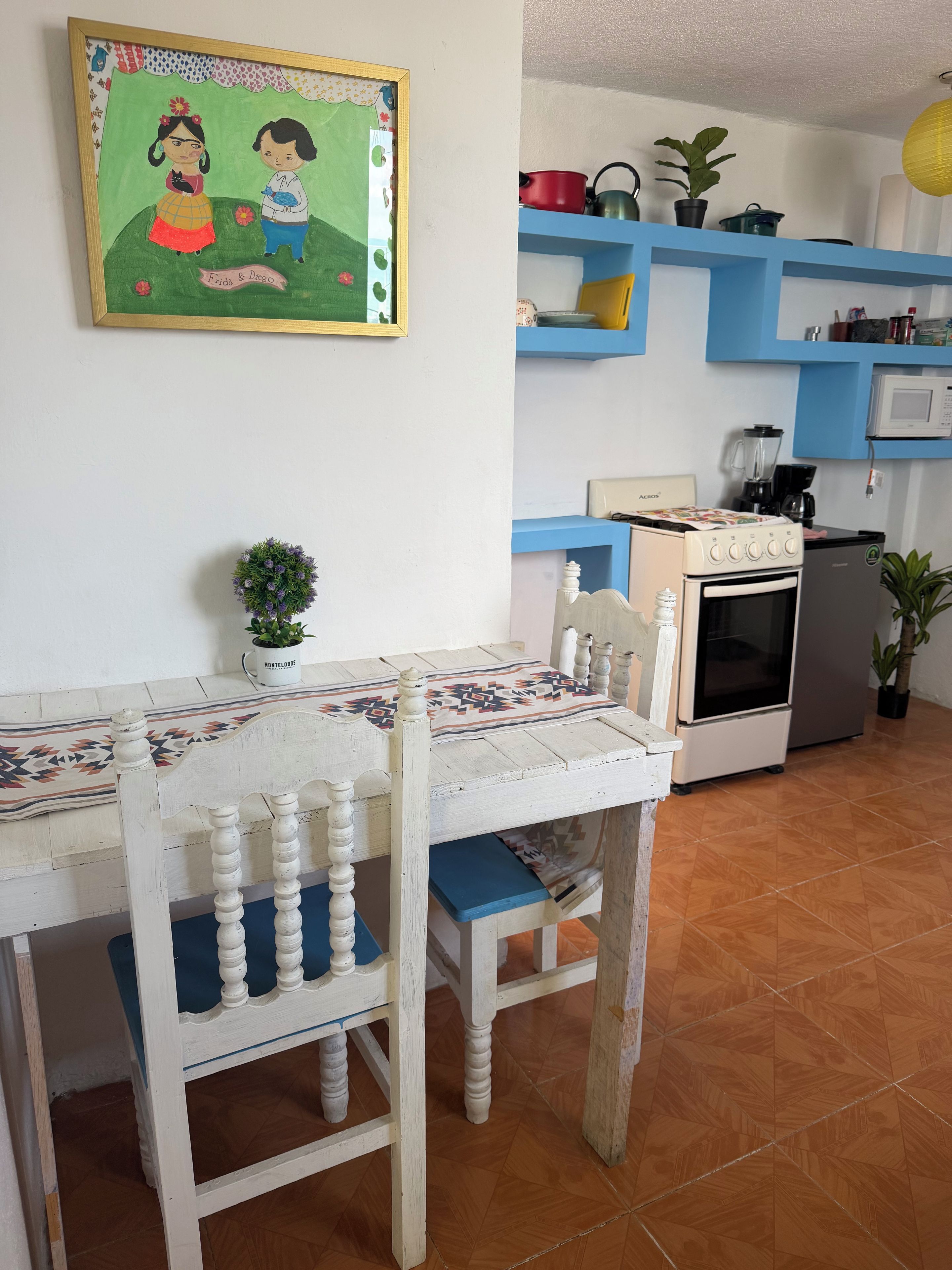 Un comedor con mesa y sillas, una cocina equipada y una pared con un cuadro enmarcado.