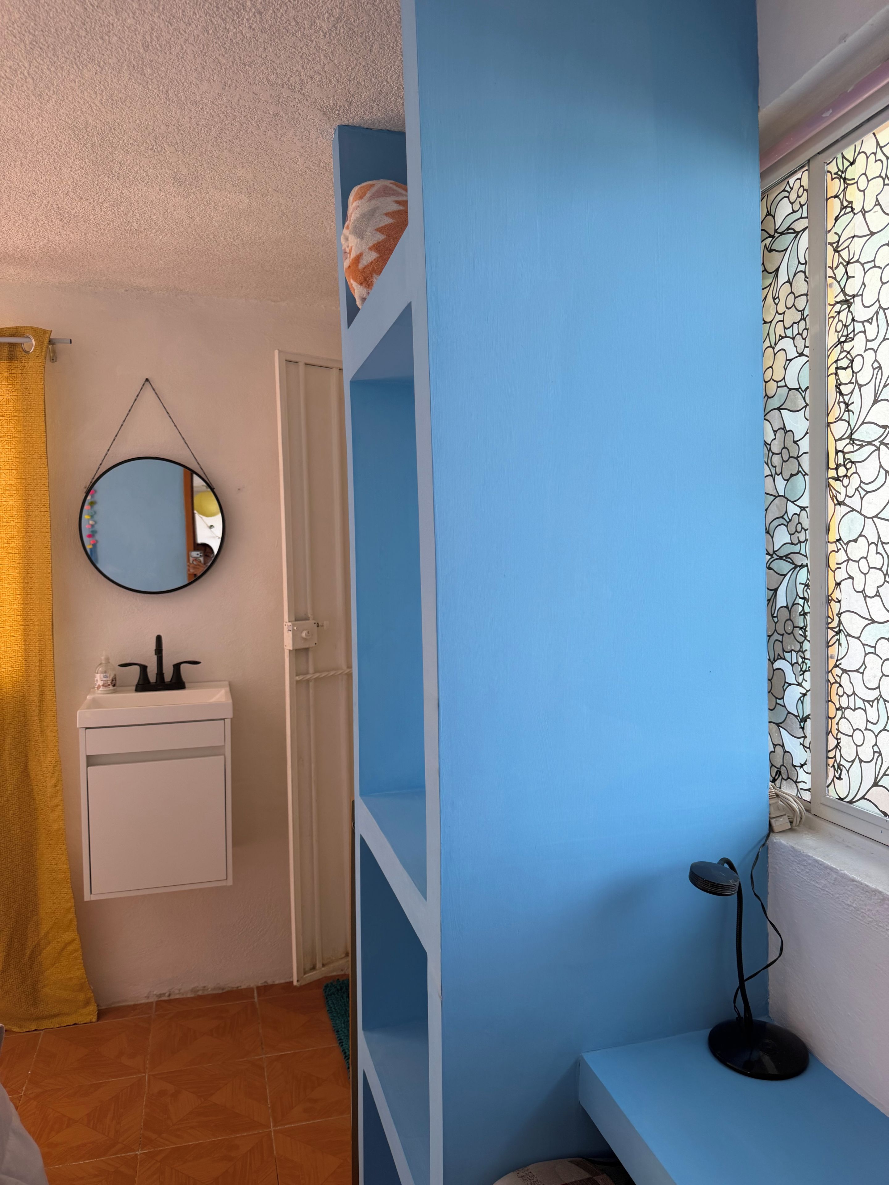 Un baño con lavamanos, espejo y ventana con diseño floral.