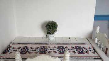A dining table with a patterned tablecloth, white chairs, a small potted plant, and a framed artwork on the wall.