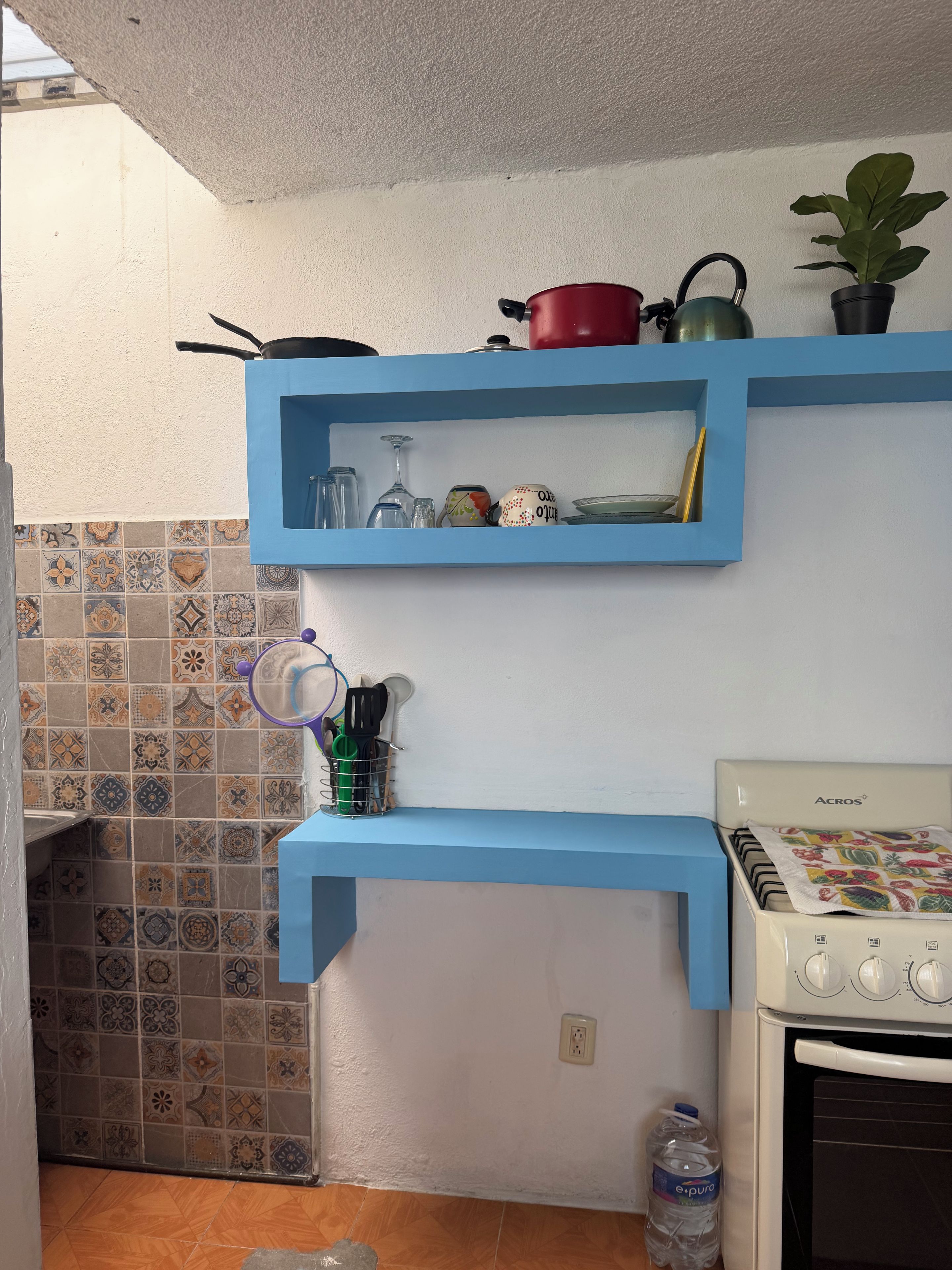A kitchen with blue shelves holding kitchenware, a water bottle, and a stove.