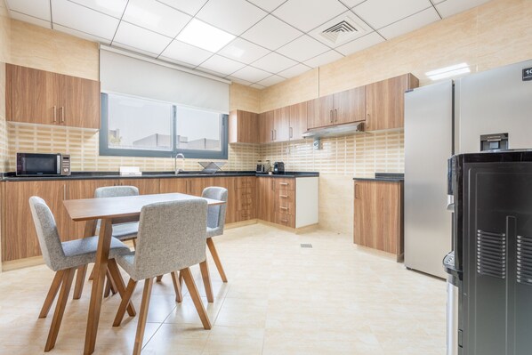 A modern kitchen with wooden cabinets, a dining table with chairs, a refrigerator, and a window providing natural light.