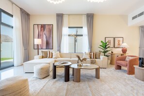 A modern living room with a sofa, armchairs, a coffee table, and a large window with curtains.