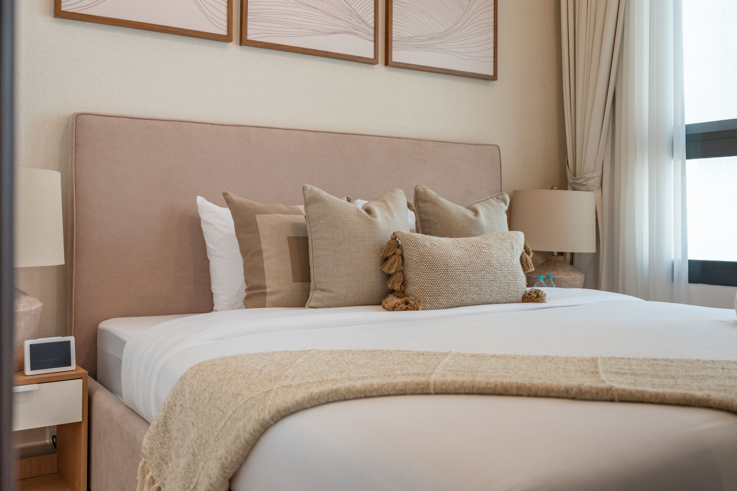 A neatly made bed with a headboard, multiple pillows, a bedside lamp, and a small bedside table with a remote control.