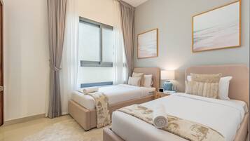 Quarto de hotel com duas camas, uma janela grande com cortinas, uma obra de arte pendurada na parede e uma mesa de cabeceira com abajur e garrafas de água.
