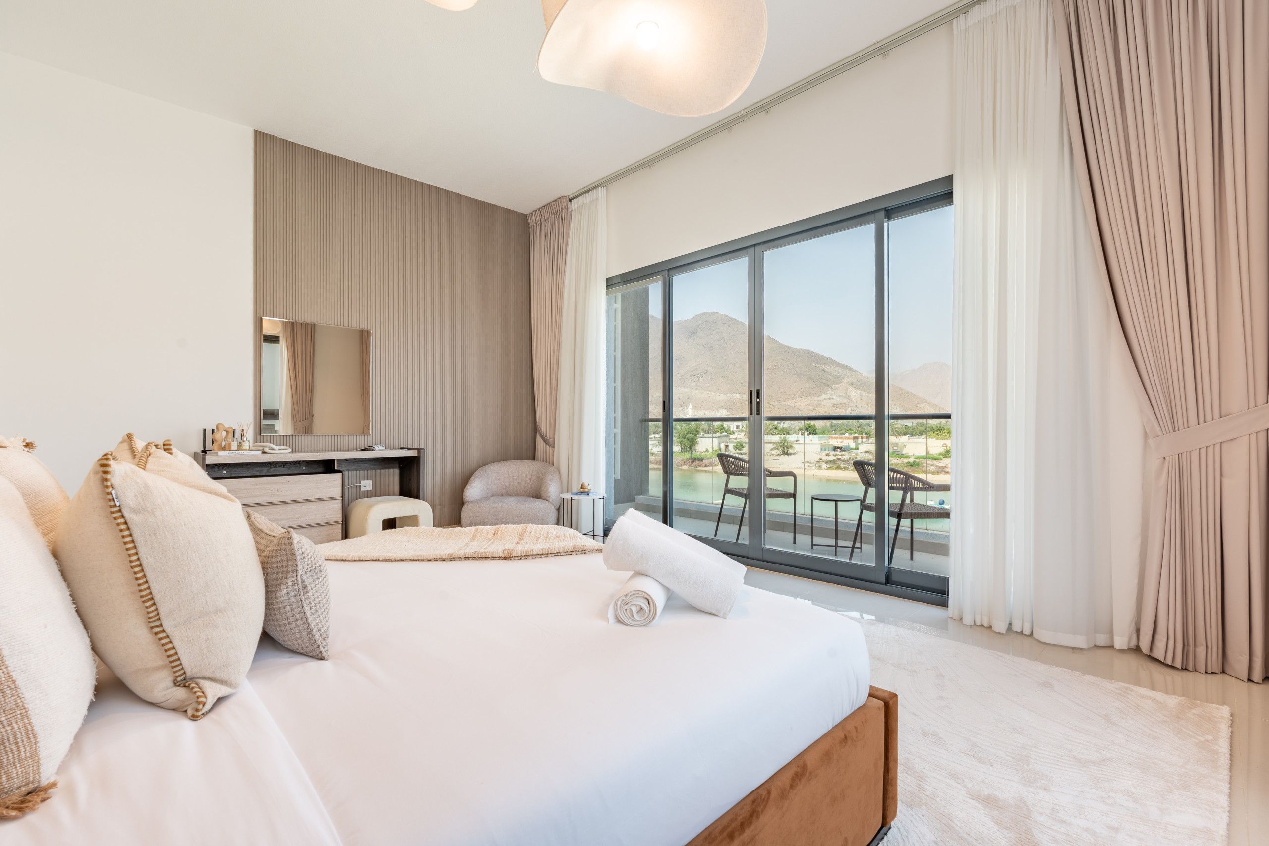 Habitación de hotel con una cama grande, un escritorio, una silla y un balcón con vistas a las montañas.