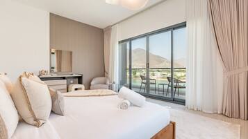 Habitación de hotel con una cama grande, un escritorio, una silla y un balcón con vistas a las montañas.