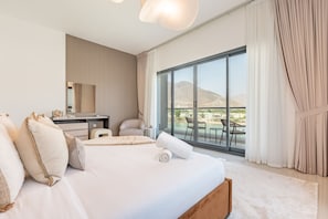 Et hotelværelse med en stor seng, et skrivebord, en stol og en balkon med udsigt til bjergene.