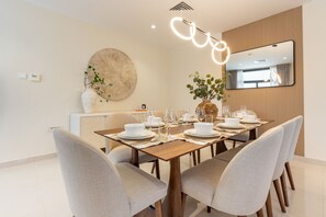 A modern dining area with a wooden table set for four, surrounded by upholstered chairs.