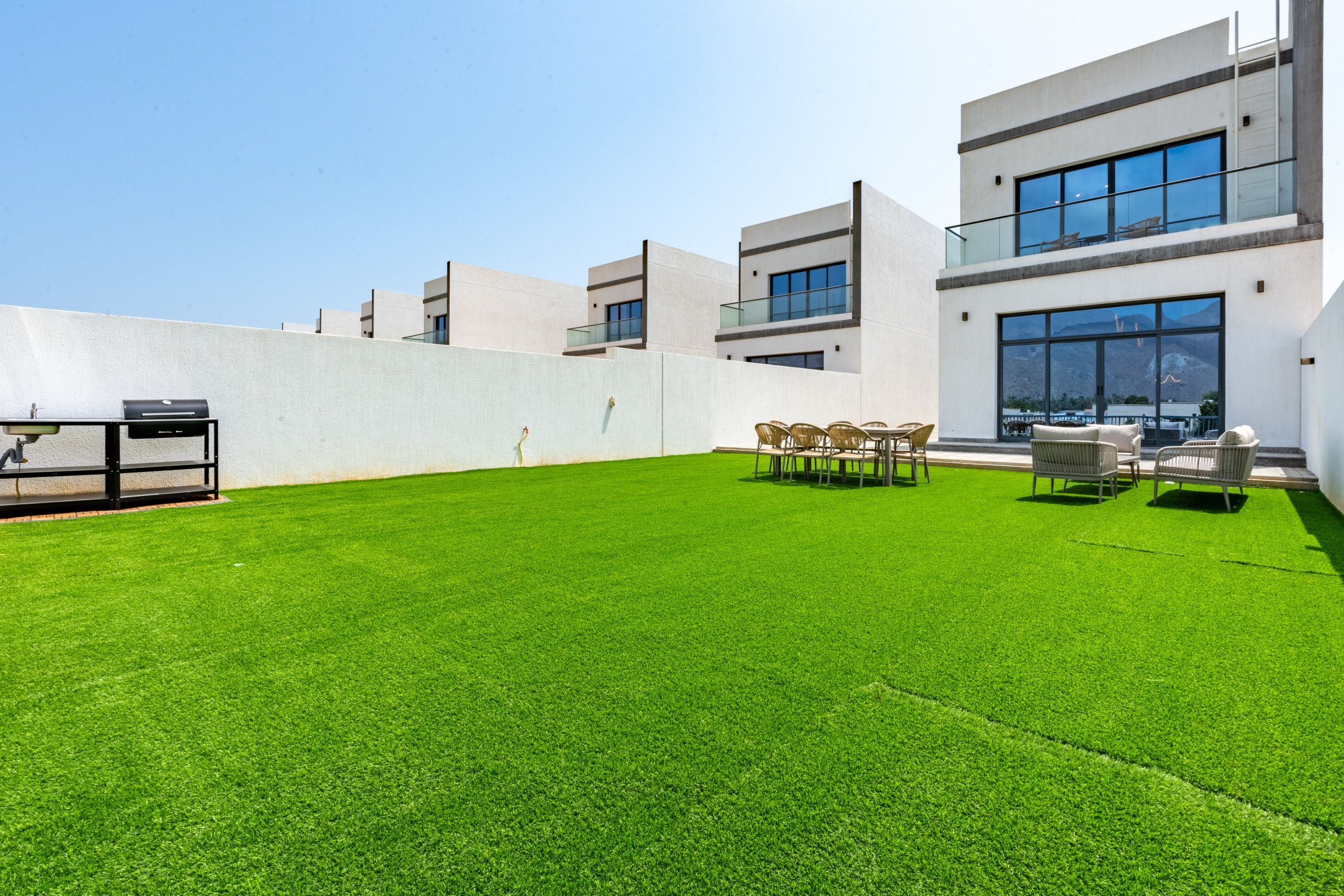 Eine Dachterrasse mit künstlichem Rasen, Gartenmöbeln und einem Grill.