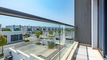 Un edificio moderno con un balcón de vidrio que da a un estacionamiento y una hilera de edificios parecidos.