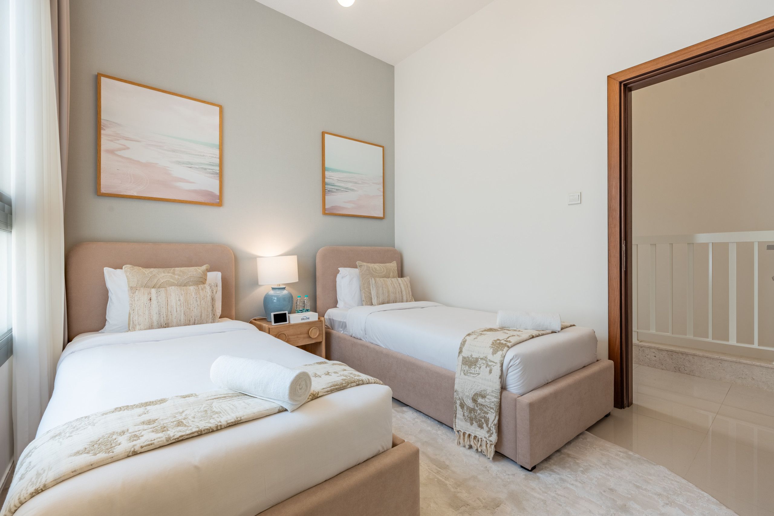 Una camera d'albergo con due letti, un comodino con una lampada e due quadri appesi al muro.
