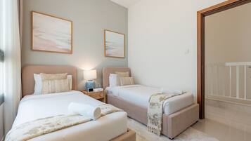 Una camera d'albergo con due letti, un comodino con una lampada e due quadri appesi al muro.