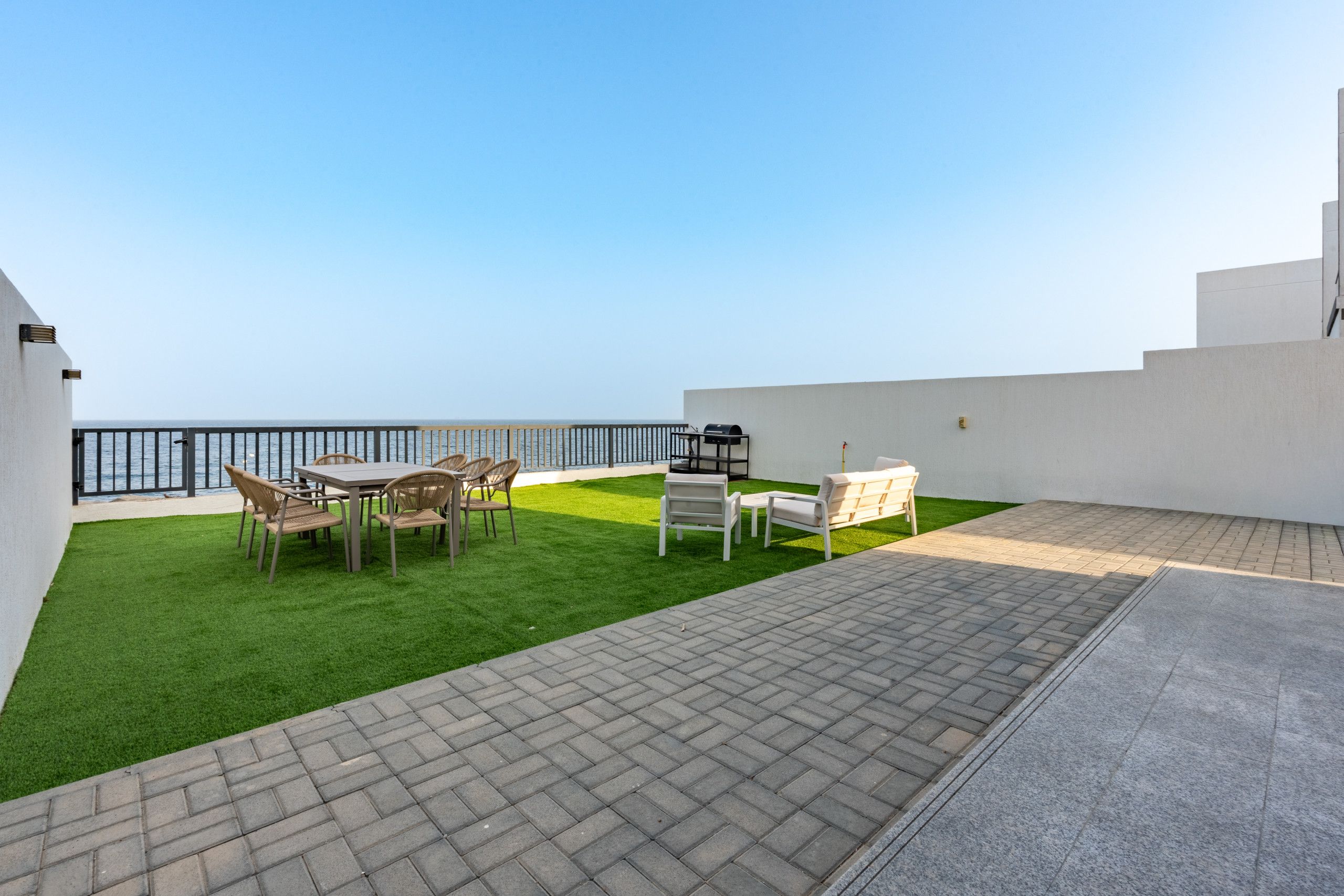 Una terraza en la azotea con vistas al mar, una zona de barbacoa y mobiliario de exterior.
