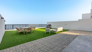 Una terraza en la azotea con vistas al mar, una zona de barbacoa y mobiliario de exterior.