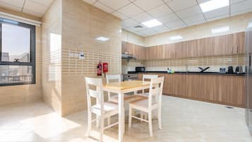 Une cuisine moderne avec une table et des chaises, un extincteur, et une vue sur la ville par une fenêtre.