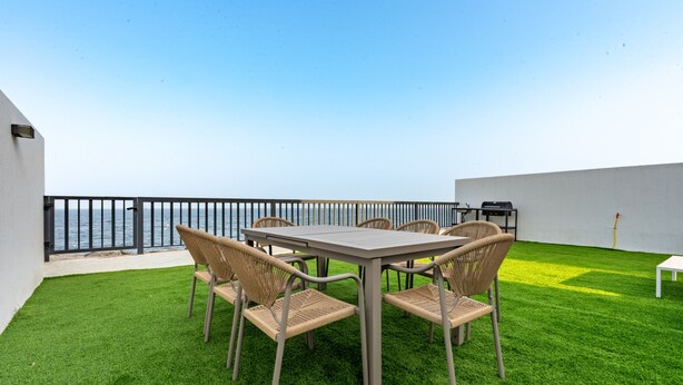 Um terraço ao ar livre com mesa, cadeiras, churrasqueira e vista para o mar.
