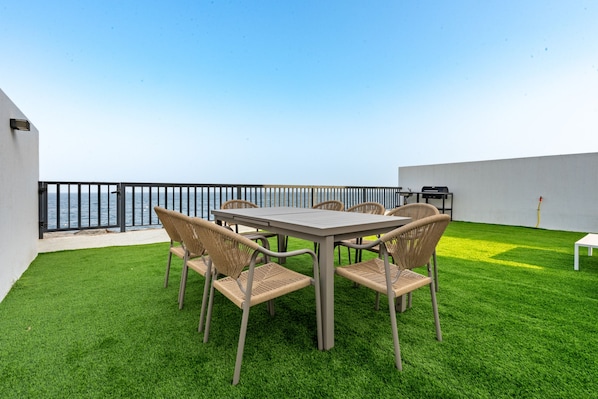 Un patio al aire libre con mesa y sillas, una parrilla y vistas al mar.