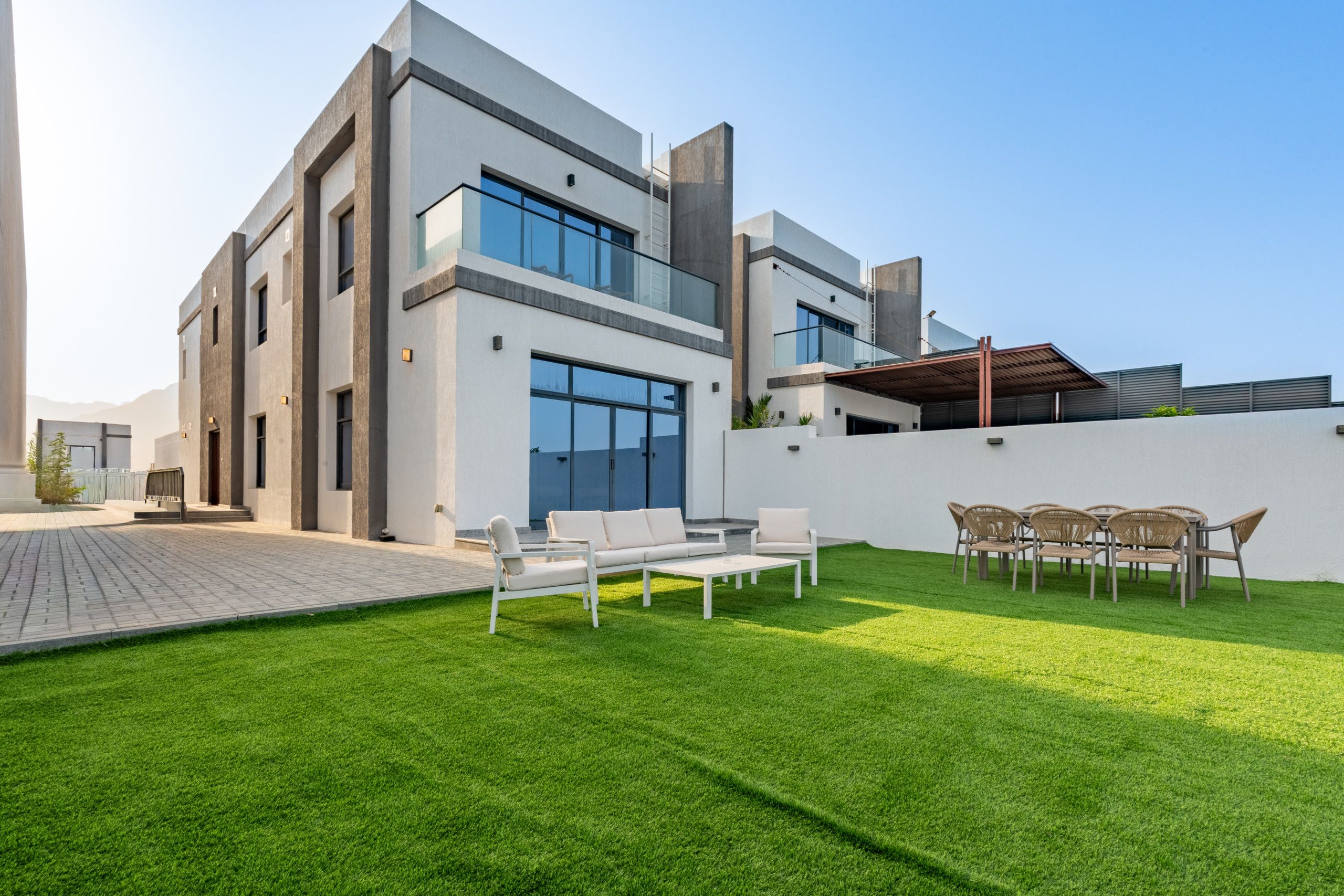 Una casa moderna de dos pisos con techo plano, ventanas amplias y césped cuidado.