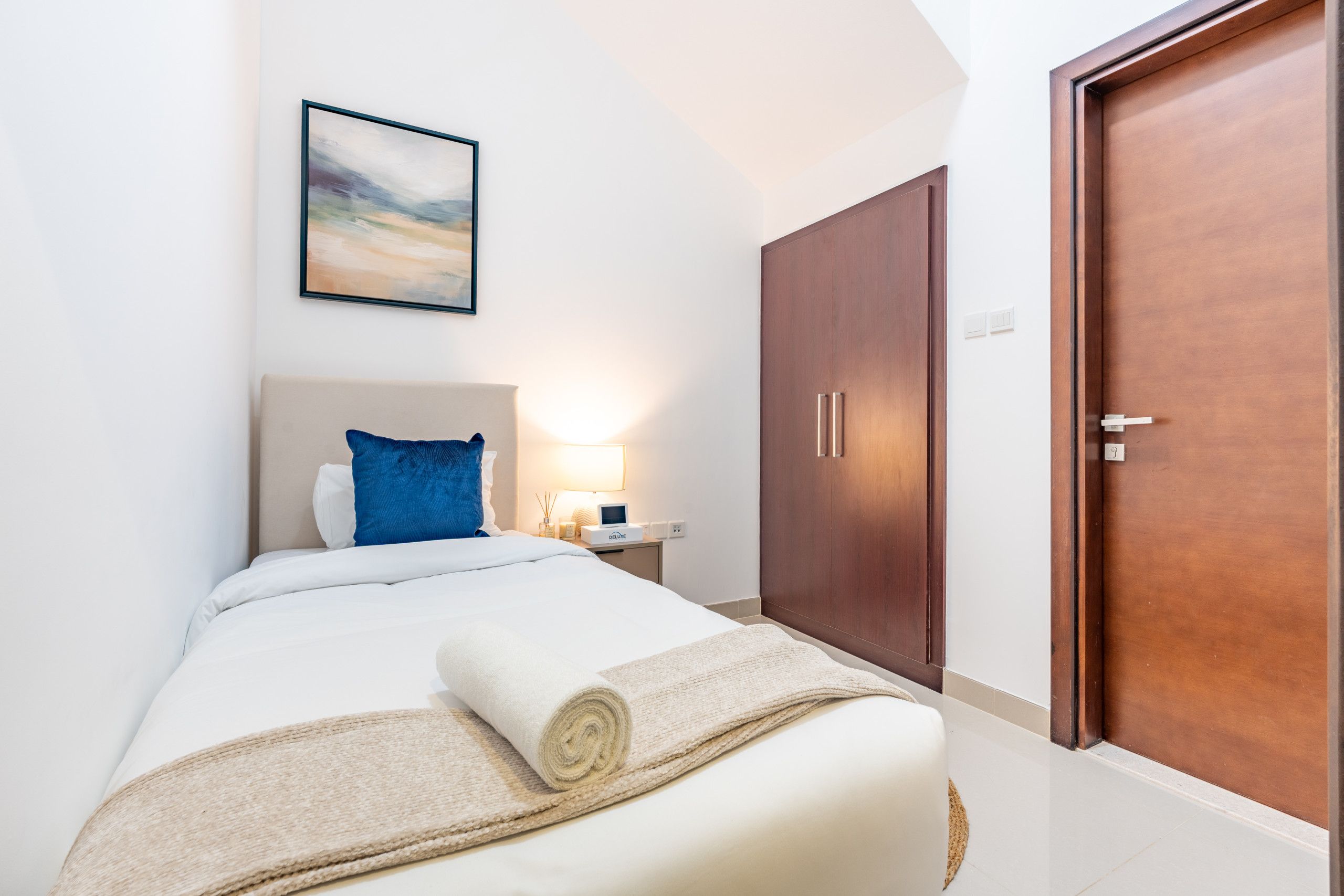 A hotel room with a bed, a nightstand, a lamp, a wooden wardrobe, and a door.