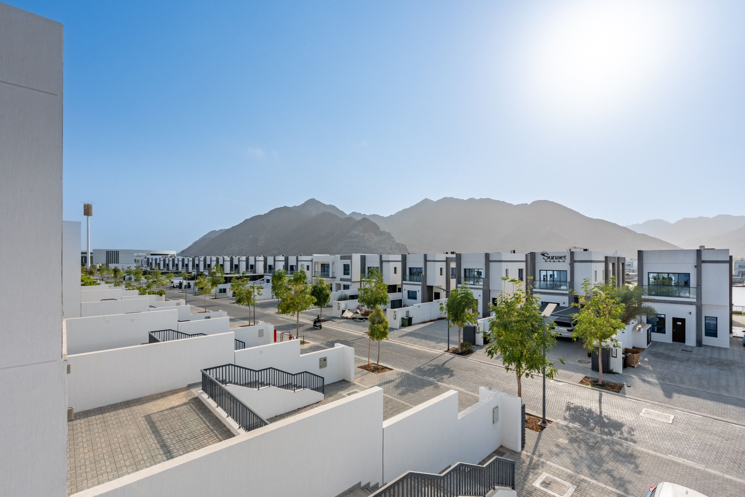 Una zona residencial moderna con edificios blancos, cielo despejado y montañas al fondo.