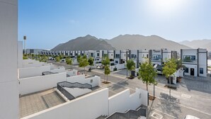 Um bairro residencial moderno com edifícios brancos, céu claro e montanhas ao fundo.
