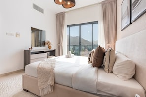 Une chambre à coucher moderne avec un grand lit, une commode, un miroir et une vue sur les montagnes par la fenêtre.