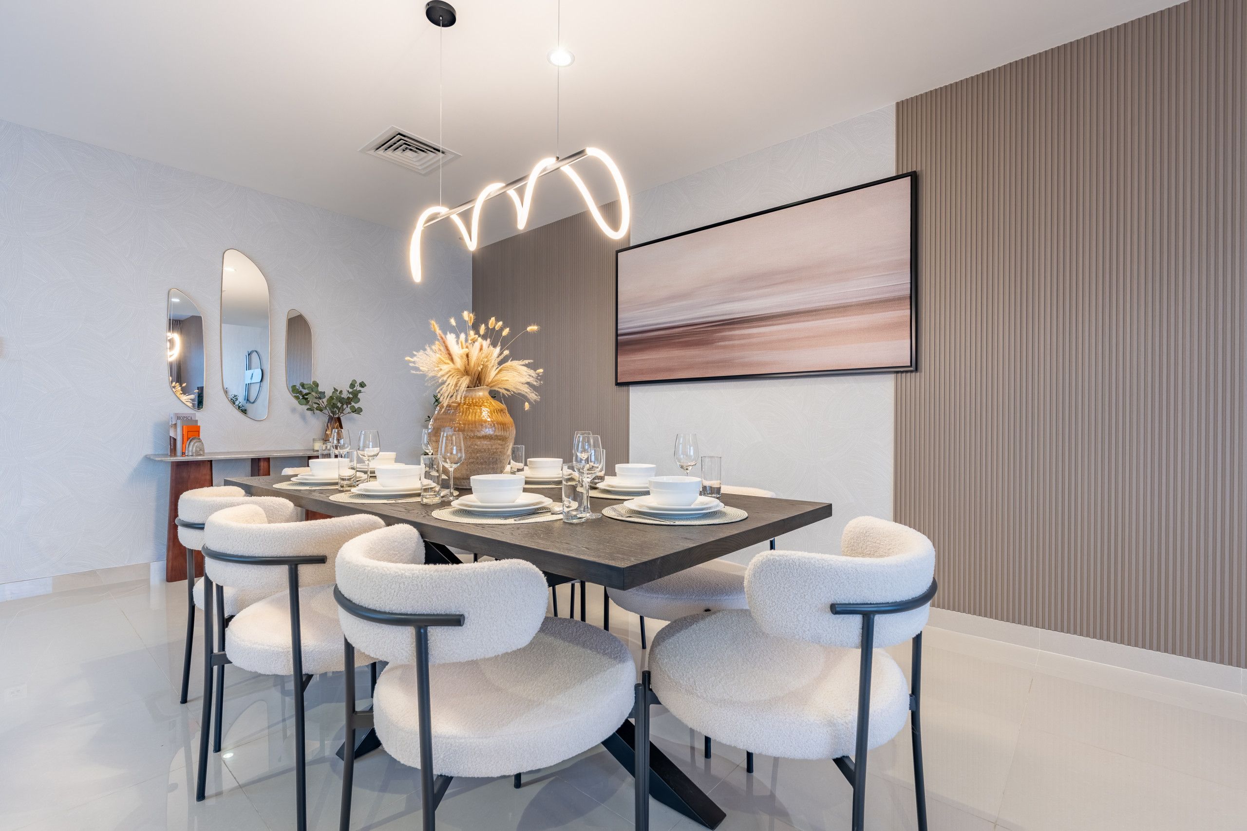Un comedor moderno con una mesa rectangular dispuesta para seis personas, rodeada de seis sillas blancas acolchadas.