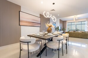 Un comedor moderno con una mesa larga, sillas blancas y un jarrón de flores secas.