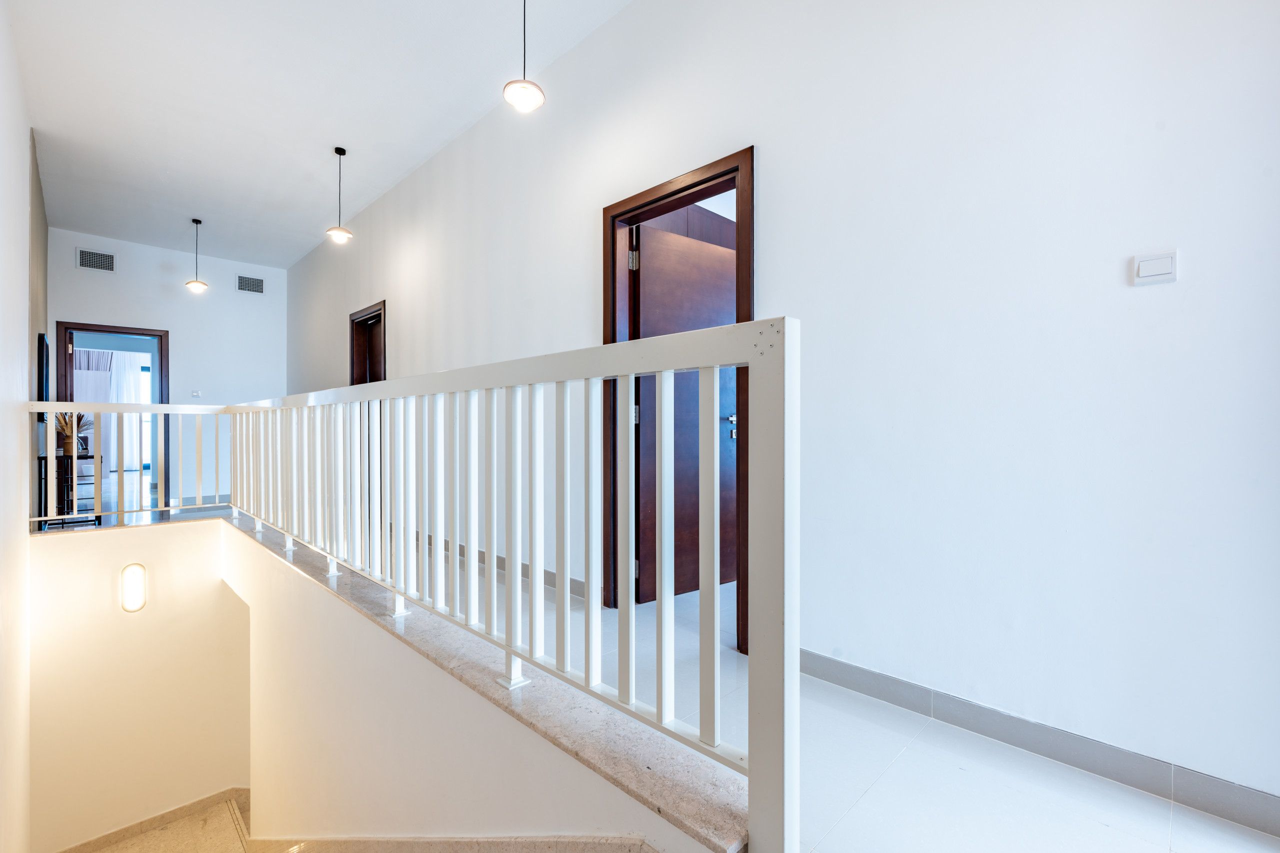 Un interior moderno con barandal blanco, una escalera y una puerta que conduce a otra habitación.
