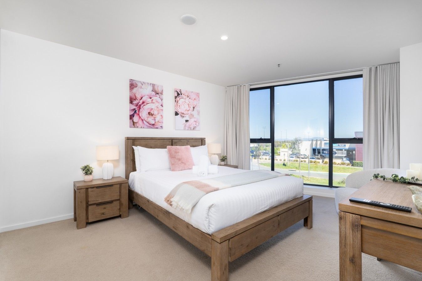 A modern bedroom with a large bed, bedside tables, a desk, and a view of the outside.