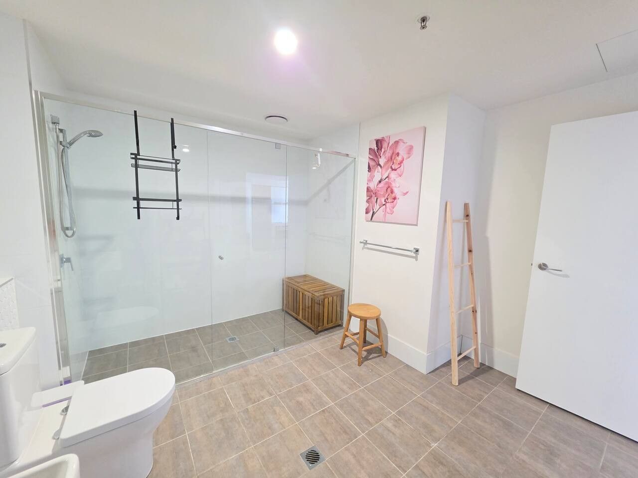 A modern bathroom with a glass shower enclosure, a wooden stool, and a ladder leaning against the wall.