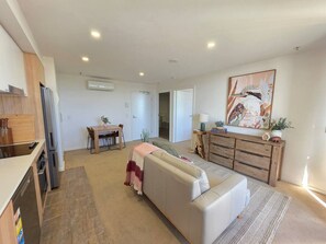 A modern living room with a sofa, a dining table, and a kitchen area with a refrigerator. - Gungahlin 1BR with Balcony, Pool, Gym and Spa (Gungahlin)
