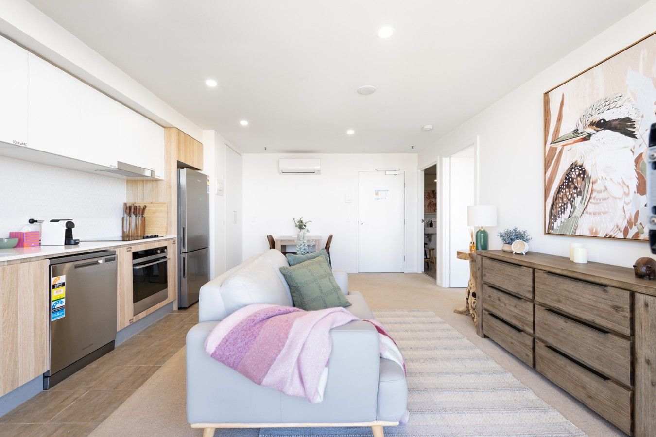 A modern kitchen with built-in appliances, a dining area with a table and chairs, and a living room with a sofa and a painting on the wall.