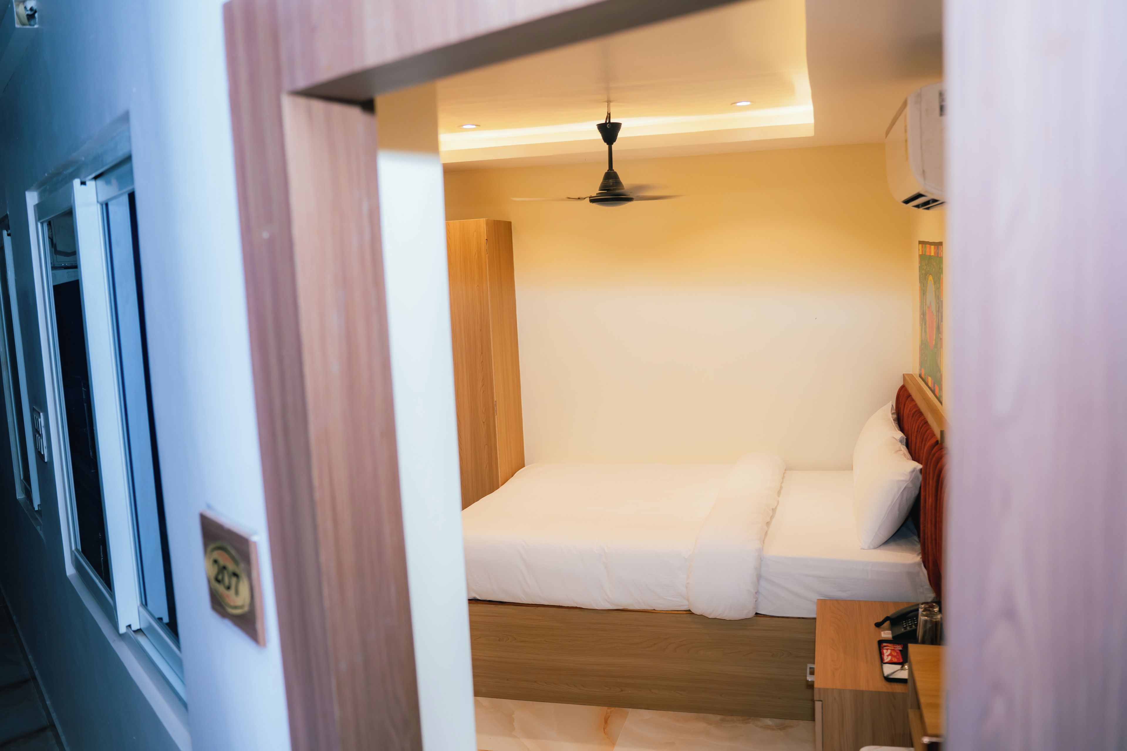 Une chambre d’hôtel avec un lit, une armoire en bois et un ventilateur de plafond.