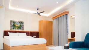 Una habitación de hotel moderna con una cama, un armario de madera, un ventilador de techo, una mesa con cubierta de mármol y un sofá azul.