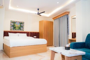 Una habitación de hotel moderna con una cama, un armario de madera, un ventilador de techo, una mesa con cubierta de mármol y un sofá azul.
