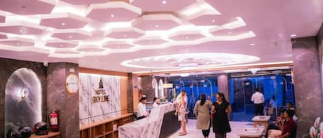 A hotel lobby with a marble reception desk, a clock, and a fire extinguisher on the wall.