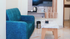 A modern living room with a teal sofa, a flat-screen TV mounted on a marble wall, a coffee table, and a small wooden cabinet.