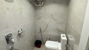 A small, enclosed shower area with a handheld showerhead, a toilet, and a wall-mounted water heater.