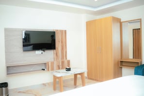 A bedroom with a bed, a wooden wardrobe, a television mounted on a marble wall, and a small wooden table.