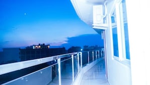 A balcony with a glass railing overlooking a cityscape at dusk.