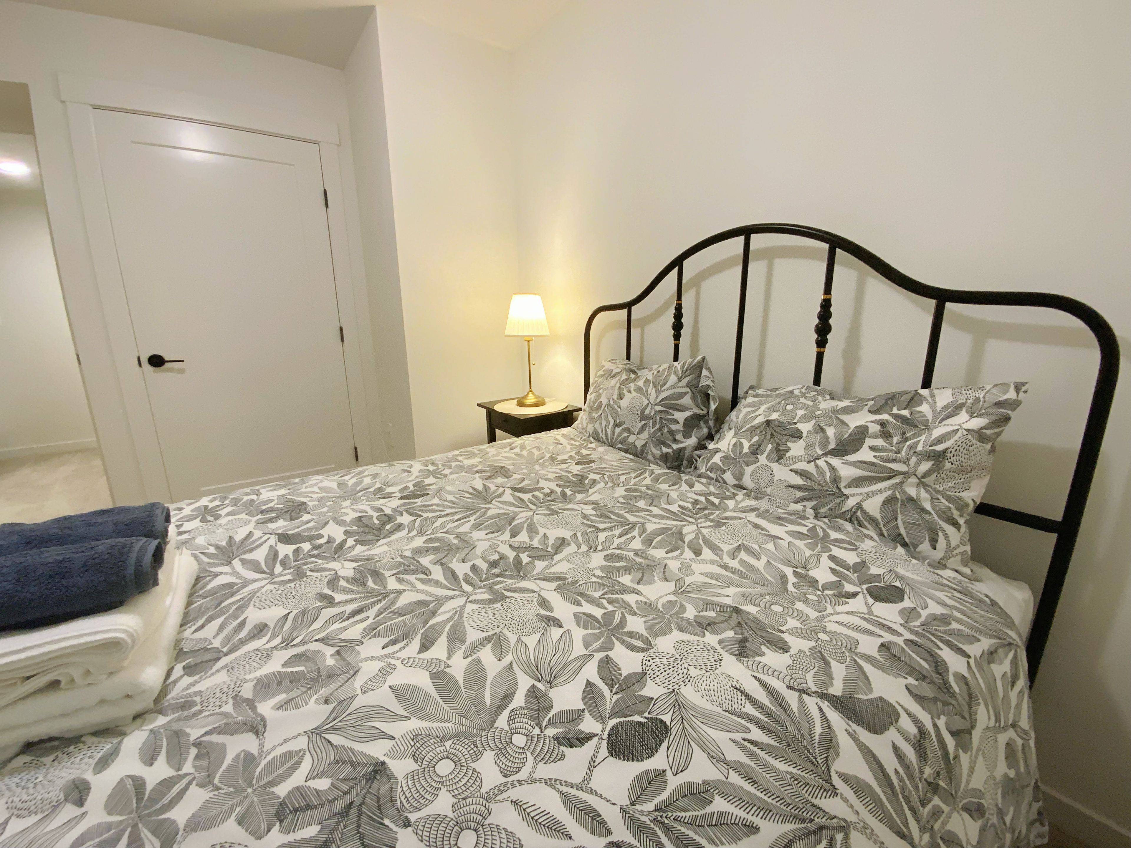 A bed with a floral-patterned bedspread, a bedside lamp, and a blue towel on a chair.