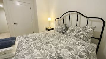 A bed with a floral-patterned bedspread, a bedside lamp, and a blue towel on a chair.