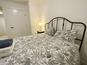 A bed with a floral-patterned bedspread, a bedside lamp, and a blue towel on a chair.