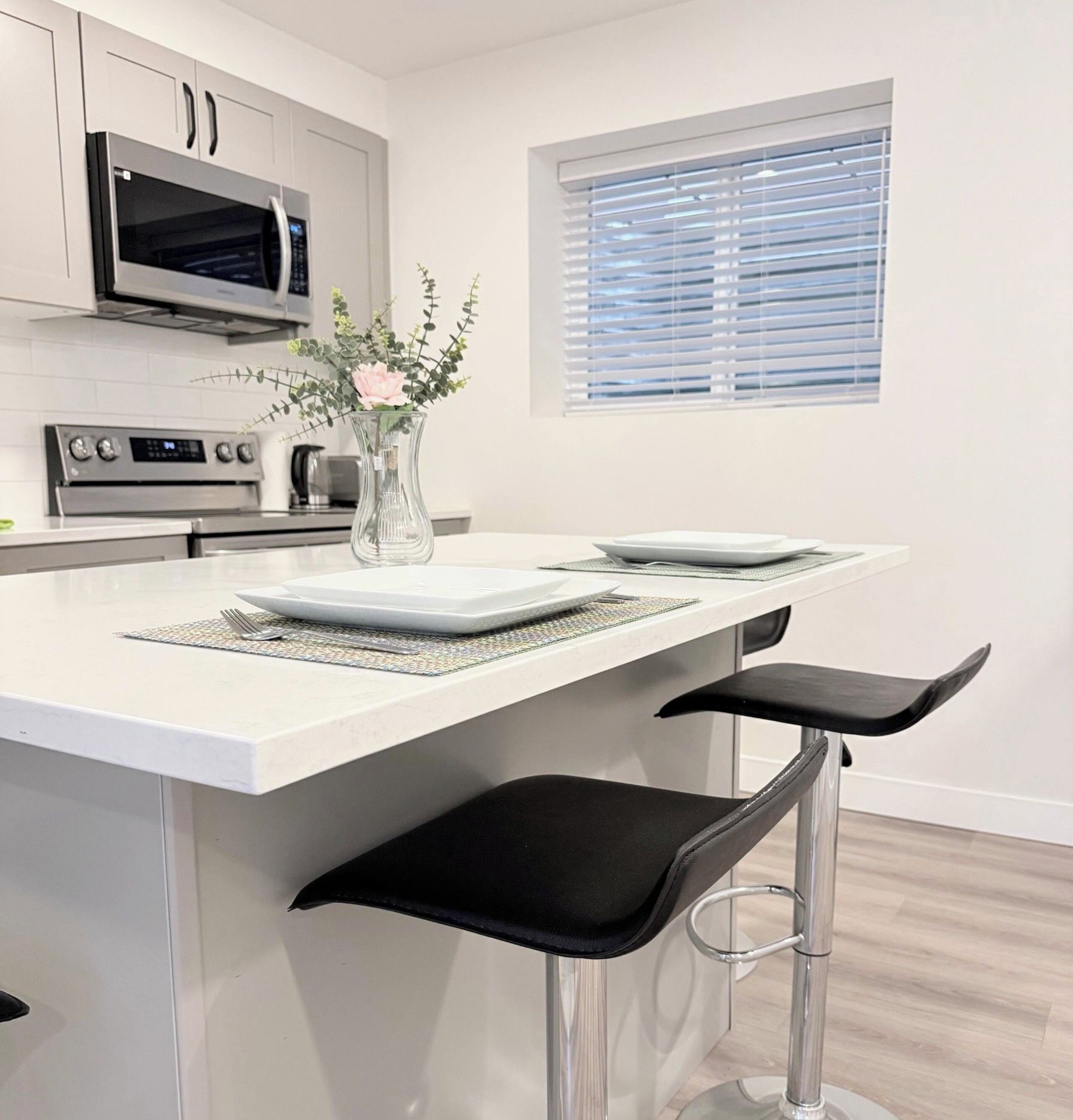 A modern kitchen with a white countertop, stainless steel appliances, and a window with blinds.