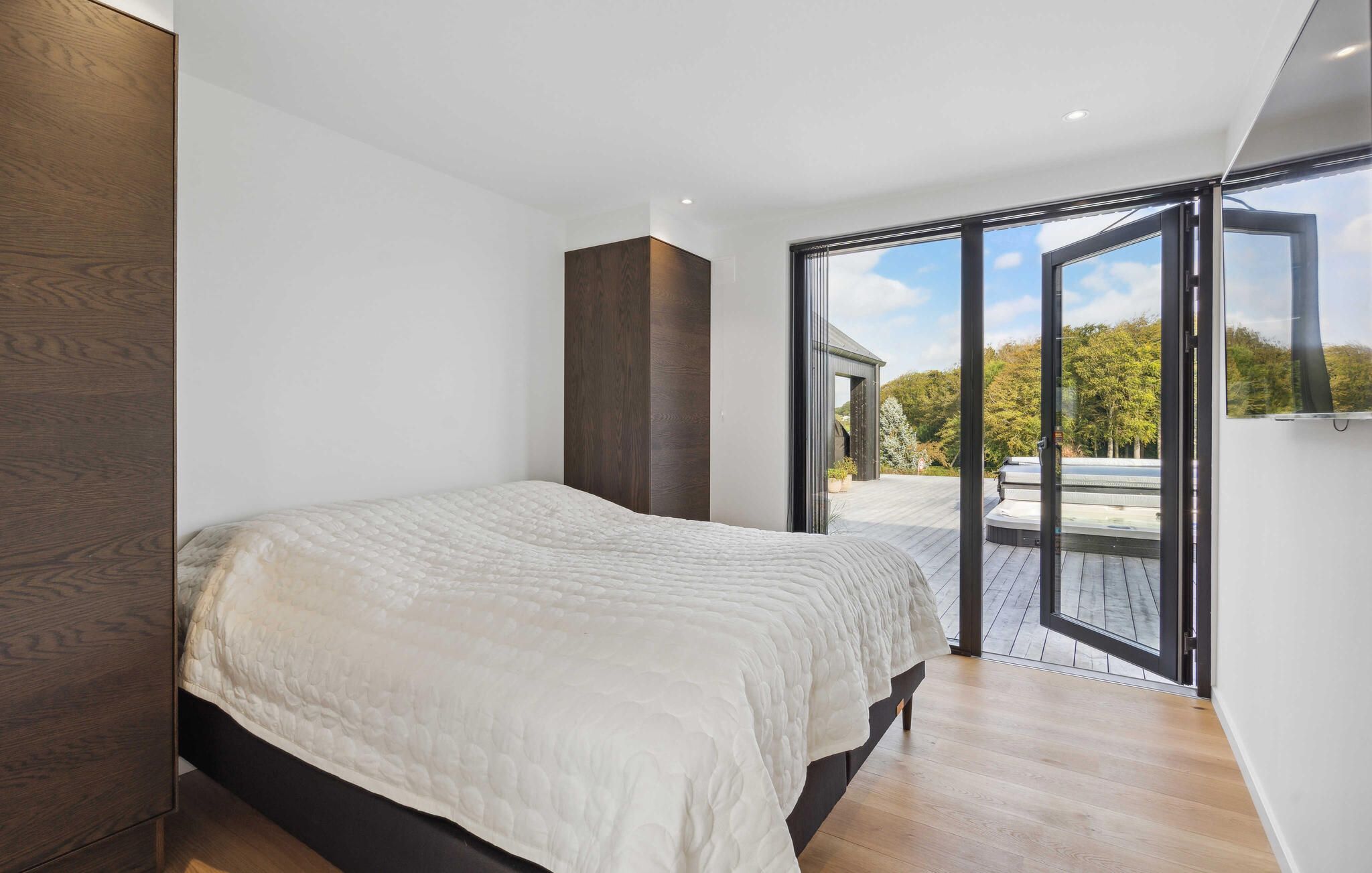 A bedroom with a large bed, a sliding glass door leading to an outdoor area, and a view of trees.