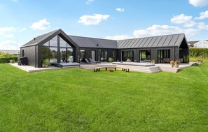 Ein modernes Haus mit großer Glasfassade, Sitzgelegenheit im Freien und einem gepflegten Rasen.