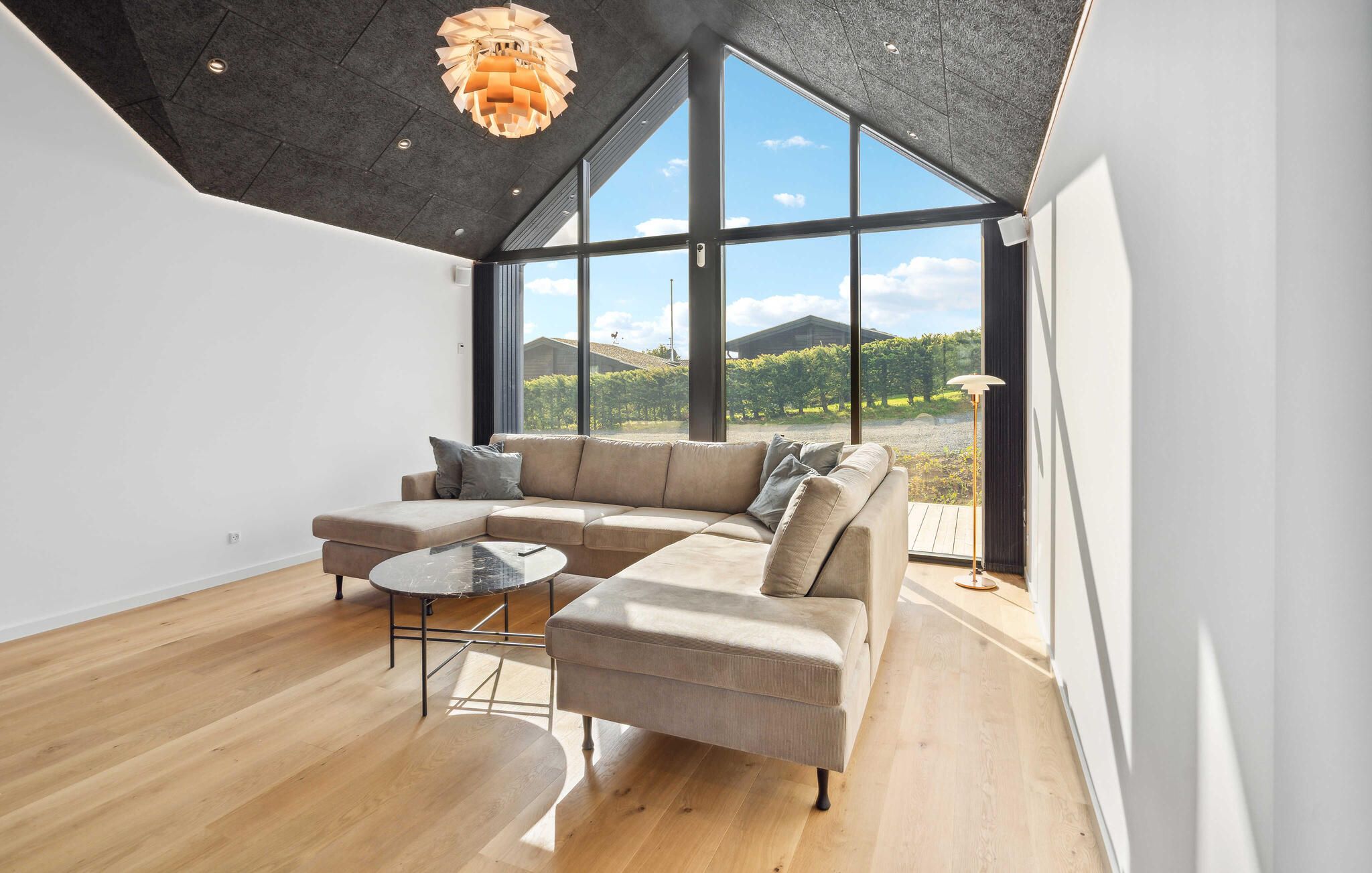 A modern living room with a sectional sofa, a small round table, and a large window offering a view of a vineyard.
