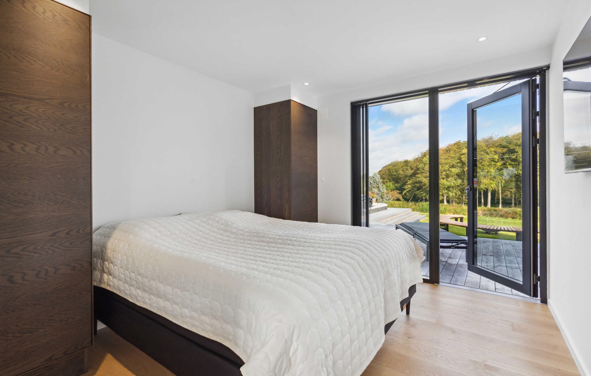 Een moderne slaapkamer met een groot bed, een houten garderobe en een glazen schuifdeur naar een buitengebied.
