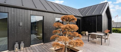 Een modern gebouw met een houten terras, een eethoek en een groot raam.